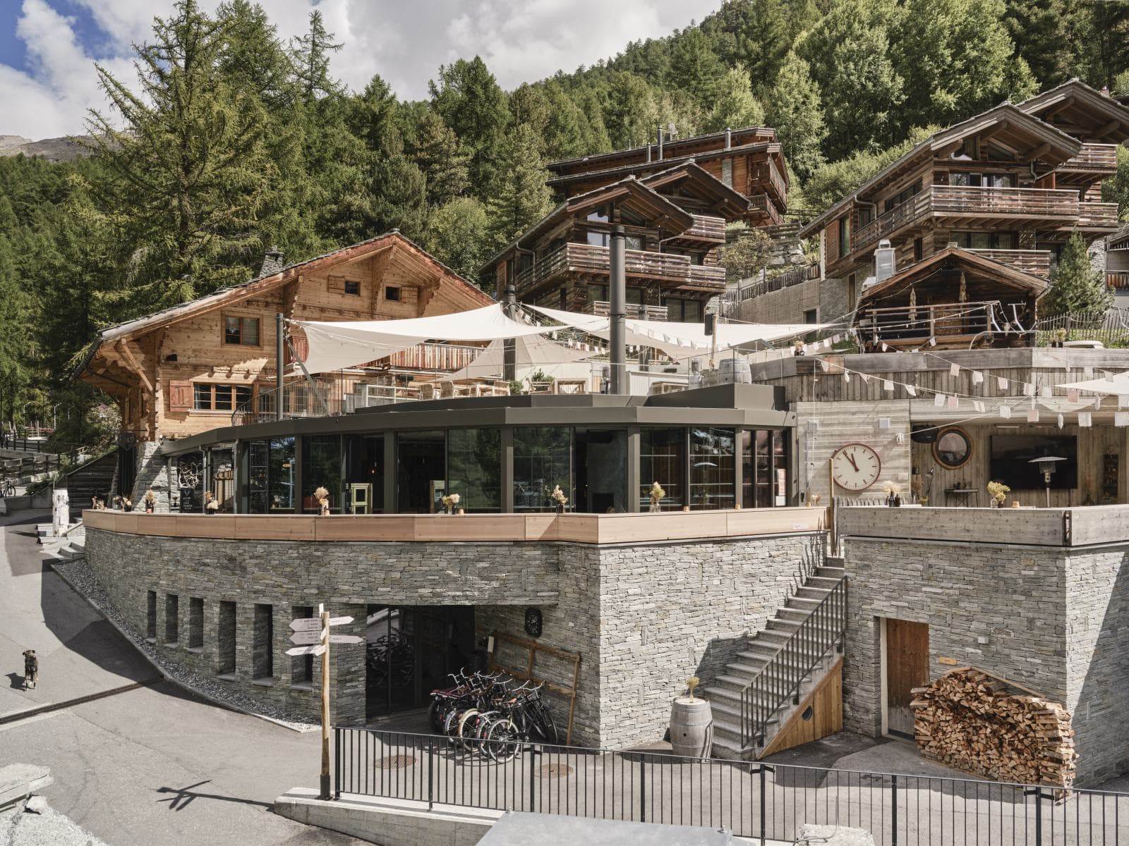 Moderne Glasstruktur in stufenweiser Terrassen- Hanglage, integriert in traditionelle Chaletarchitektur aus Holz und Stein.