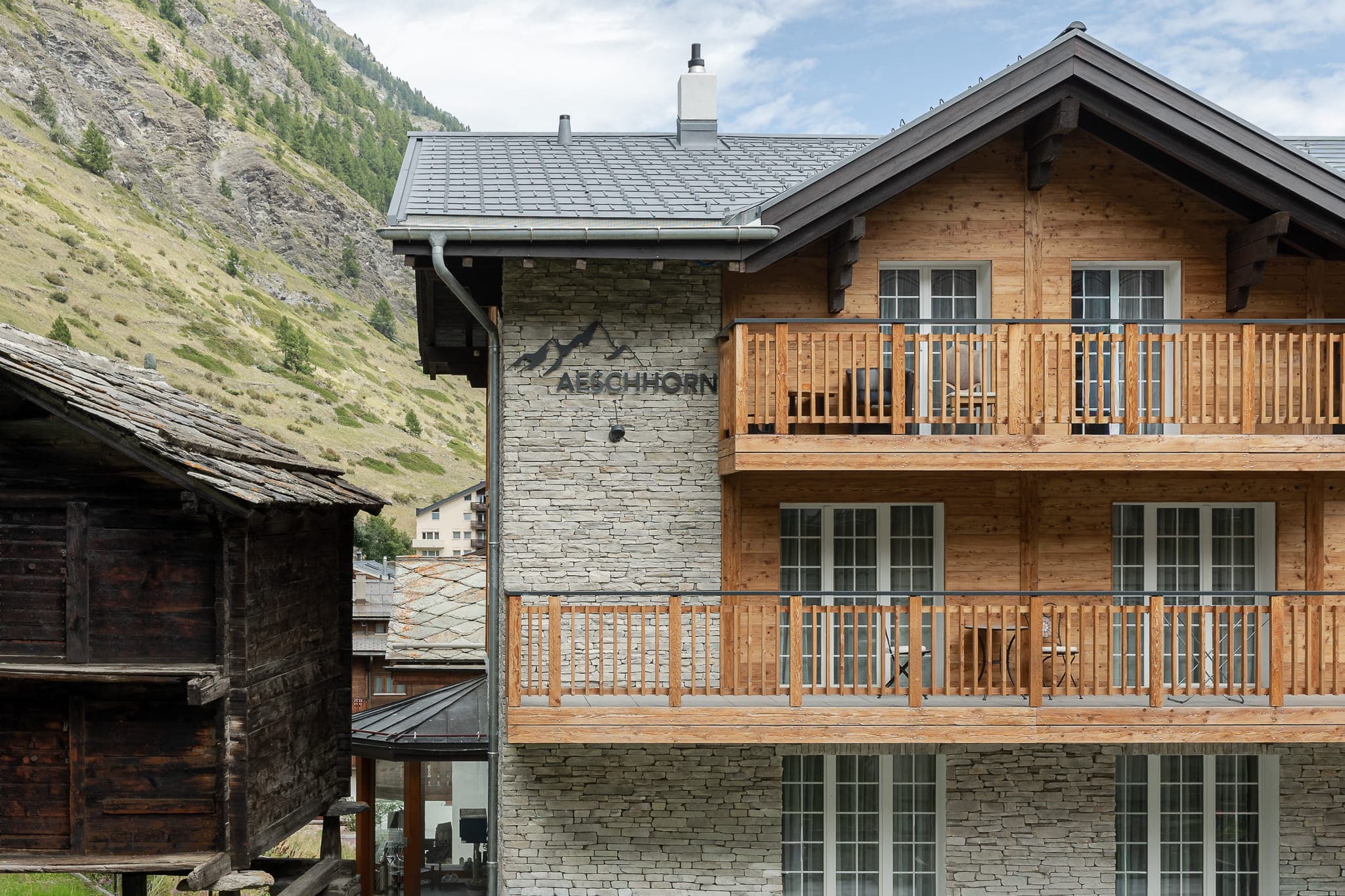 Fassadenansicht des Chalet Aeschhorn in Zermatt mit Naturstein- und Holzfassade, Holzbalustraden an Balkonen.